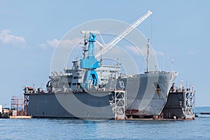 Large iron navy ships in shipyard for repair. Big crane in dockyard. Blue sea harbor