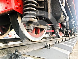 Large iron wheels of a red and black train standing on rails and suspension elements with springs of an old industrial steam