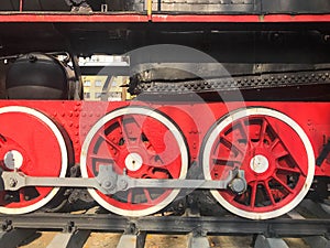 Large iron wheels of a red and black train standing on rails and suspension elements with springs of an old industrial steam