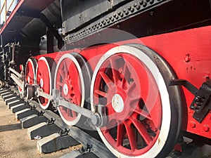 Large iron wheels of a red and black train standing on rails and suspension elements with springs of an old industrial steam