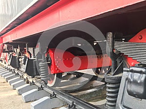 Large iron wheels of a red and black train standing on rails and suspension elements with springs of an old industrial steam