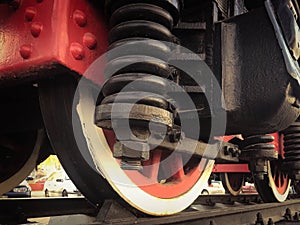 Large iron wheels of a red and black train standing on rails and suspension elements with springs of an old industrial steam