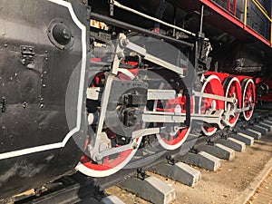 Large iron wheels of a red and black train standing on rails and suspension elements with springs of an old industrial steam