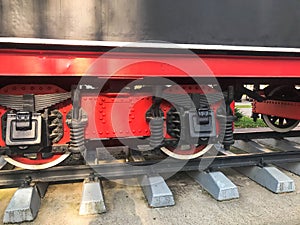 Large iron wheels of a red and black train standing on rails and suspension elements with springs of an old industrial steam