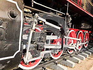 Large iron wheels of a red and black train standing on rails and suspension elements with springs of an old industrial steam