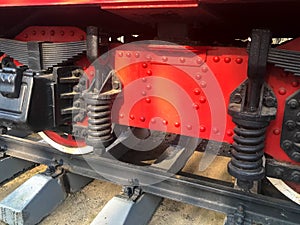 Large iron wheels of a red and black train standing on rails and suspension elements with springs of an old industrial steam