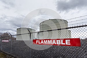 Large jet fuel or oil storage tanks behind a chain link fence with warning signs