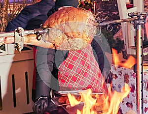 Large juicy pork leg roasting on a spit over an open fire at a farmers market on a winter evening.