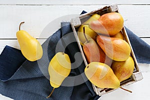 Large juicy yellow pears in a rustic wooden fruit box on a white table.