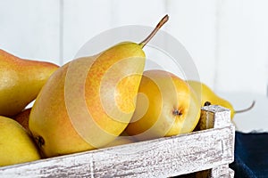 Large juicy yellow pears in a rustic wooden fruit box on a white table.