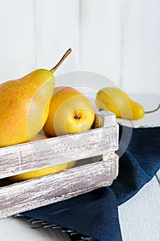 Large juicy yellow pears in a rustic wooden fruit box on a white table.