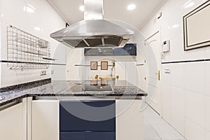 Large kitchen furnished with white and blue furniture, polished black granite countertop with an island with a stainless steel