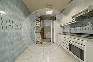 Large kitchen with gloss white wood cabinets, granite stone countertops, white built-in appliances, and ugly blue and white tile