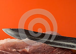 A large kitchen knife cuts a piece of raw red meat. Cutting meat. Piece of fresh pork close-up.Selective focus,