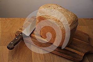 Large kitchen knife and homemade bread on a numbed cutting board cools down, close-up, copy space