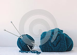 Large knitting needles are stuck into a large ball of blue yarn next to a product knitted from yarn