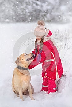 A large labrador dog and a cat in winter on a walk with a young woman in a snowy field