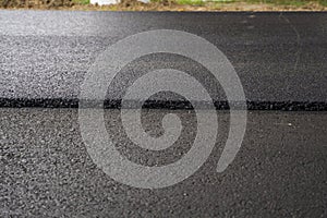 A large layer of fresh hot asphalt. Layer of asphalt raw material in a shallow depth of field. Rollers rollin fresh hot