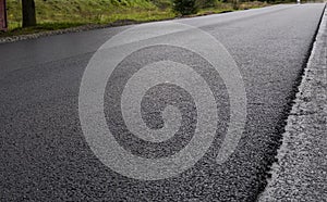 A large layer of fresh hot asphalt. Layer of asphalt raw material in a shallow depth of field. Rollers rollin fresh hot