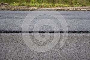 A large layer of fresh hot asphalt. Layer of asphalt raw material in a shallow depth of field. Rollers rollin fresh hot