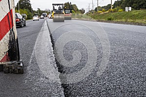 A large layer of fresh hot asphalt. Layer of asphalt raw material in a shallow depth of field. Rollers rollin fresh hot