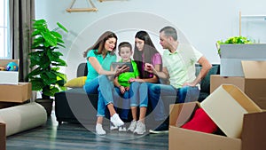 In a large living room mature charismatic parents and their kids enjoying the moment in a new house they using digital