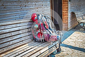 Large loaded backpack with walking sticks and water bottle and sleeping bag and child seat on wooden bench outside wooden