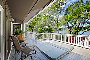 Large long balcony home exterior with hot tub and chairs, lake view.