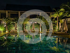 a large, long swimming pool surrounded by palm trees is illuminated with lights