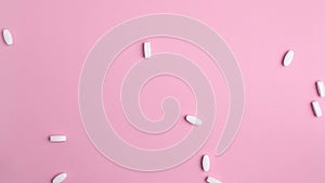 Large long white shiny tablets falling down. On pink background, close-up top view