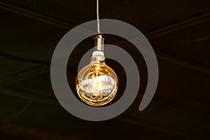 Large luminous round light bulb on a cord in a dark room