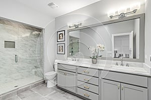 A large, luxurious bathroom with a marble shower and grey vanity.