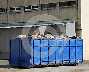 Large metal blue dumpster near the wall of the house