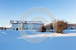 Large metal-clad white barn with metal silo in field covered in pristine fresh snow