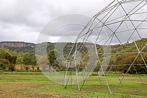 Large metal geodesic dome greenhouse structure in a rural setting with hills in the background