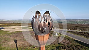 Large metallic sculpture of a torch is prominently displayed atop a pole in the foreground of a road