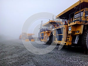 Large mining trucks are parked outside during fog.