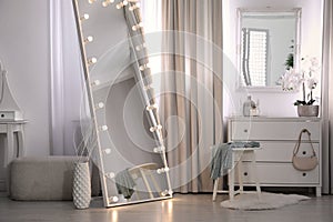 Large mirror with light bulbs and chest of drawers in stylish room. Interior design