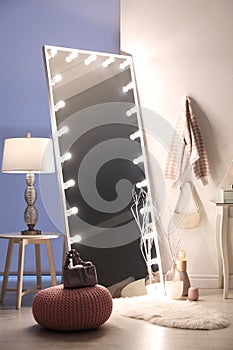 Large mirror with light bulbs and knitted pouf in stylish room. Interior design