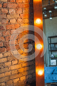 A large mirror in a wooden frame with bulbs near a brick wall