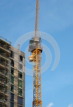 large modern building under construction covered in scaffolding with a tower crane against a bright blue sky