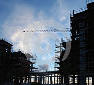 Large modern construction site in silloute with scaffolding and railings covering the structure with crane in the background