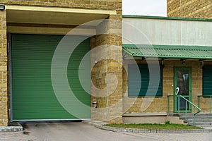 A large modern garage made of beige brick and green roller gates. Video surveillance system at the entrance to the garage. Safe