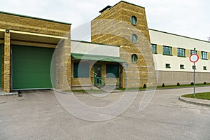 A large modern garage made of beige brick and green roller gates. Video surveillance system at the entrance to the garage. Safe