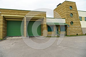 A large modern garage made of beige brick and green roller gates. Video surveillance system at the entrance to the garage. Safe