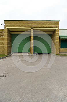 A large modern garage made of beige brick and green roller gates. Video surveillance system at the entrance to the garage. Safe