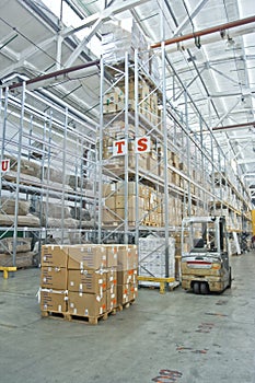 Large modern warehouse with forklifts, shelves with pallets, boxes, containers and goods