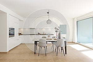 Large modern white kitchen with a marble table and four chairs in front. This is the interior of a modern flat