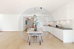 Large modern white kitchen with a marble table and four chairs in front. This is the interior of a modern flat