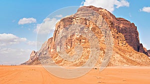 Large mountain in red desert, small 4wd vehicle in foreground for scale - typical scenery of Wadi Rum, Jordan